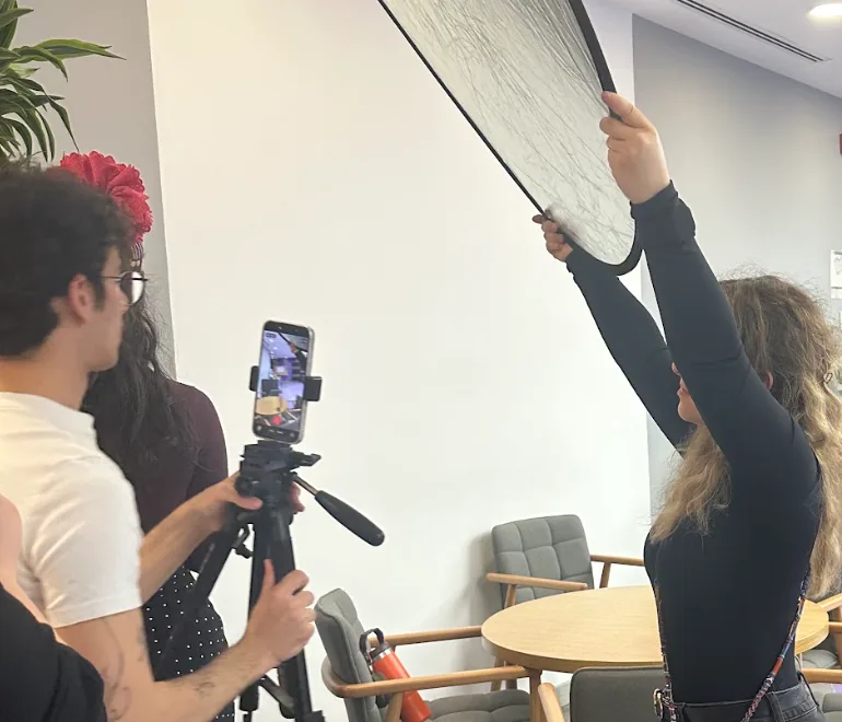 Behind the scenes at a brand shoot, a phone on a tripod and a reflector held overhead